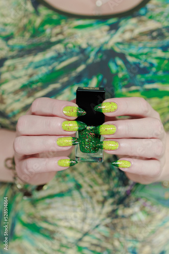 Woman's hand with long nails and bright yellow green thermo manicure with bottles of nail polish photo