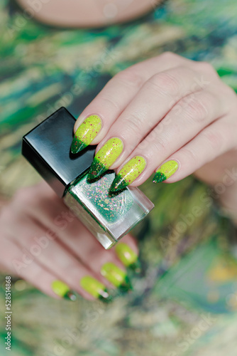 Woman's hand with long nails and bright yellow green thermo manicure with bottles of nail polish photo