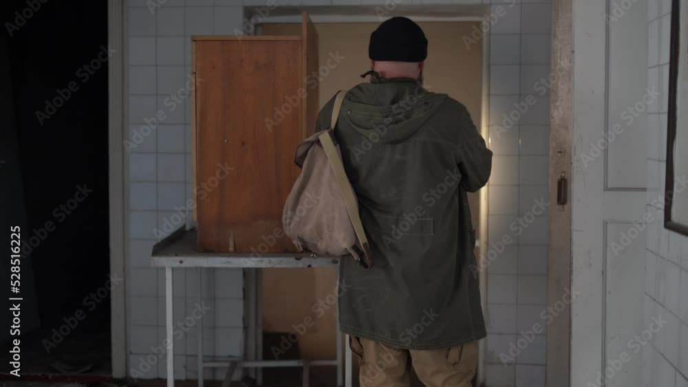 a man with a backpack walks through an old abandoned large building. concept of a survivor wandering in the post-apocalyptic world in search of food. a man with a backpack walks through an old abandoned large building. concept of a survivor wandering in the post-apocalyptic world in search of food.