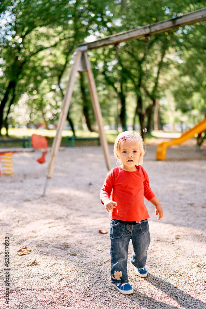 Little girl walks through the playground past the swings. High quality photo