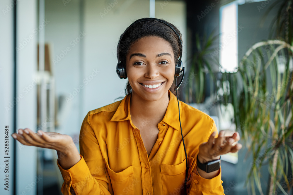 Portrait of happy black businesswoman in headset talking, gesturing and smiling at camera, sitting in office Portrait of happy black businesswoman in headset talking, gesturing and smiling at camera, sitting in office