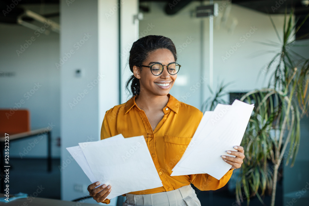 Successful entrepreneurship. Happy african american businesswoman checking financial papers in office Successful entrepreneurship. Happy african american businesswoman checking financial papers in office