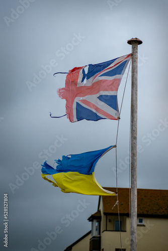 Ripped and tatty Union jack flag and Ukrainian flag fly together. Shredded and worn out they fly together in unity. Symbolic of adversity and resistance. Colorful flags together. Friends and allies photo