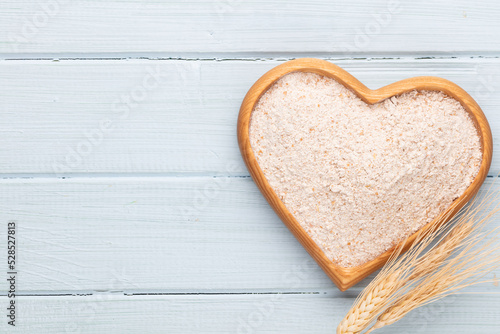 Wheat flour in a wooden heart shape bowl on a pastel background.