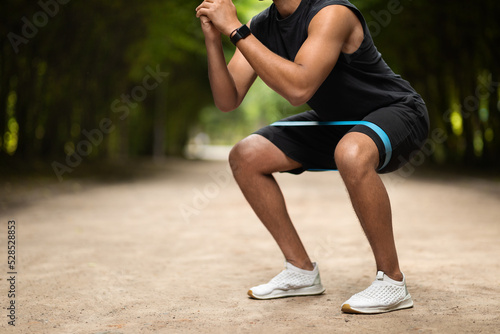 Unrecognizable muscular black man exercising in the park, using band