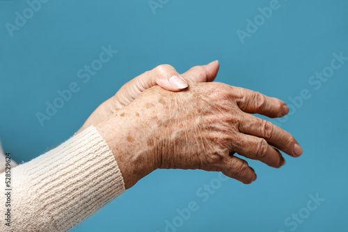 A senior woman is doing a brush massage, experiencing pain. Blue background, hands close-up. The concept of rheumatism and arthritis photo