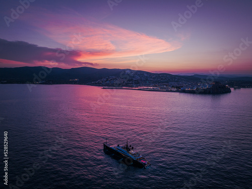 Vista aérea de un atardecer en peñíscola con un megayate en primer plano y el castillo y nubes rojas al fondo.