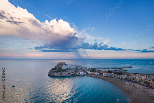 Fotografía aérea de Peñíscola al atardecer con nubes y lluvia en el fondo.