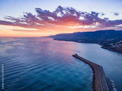 Fotografía de la escollera del puerto de Peñíscola durante el atardecer con la sierra de Irta y nubes al fondo