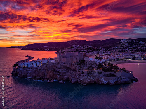 Fotografía aérea del castillo de Peñíscola durante un atardecer con nubes rojas.