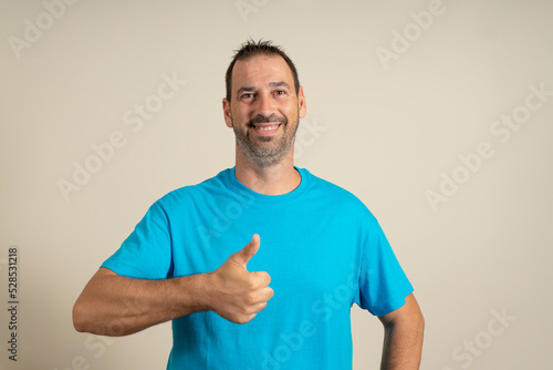 Adult hispanic man over isolated background doing happy thumbs up gesture with hand. Approving expression looking at camera showing success © Andres