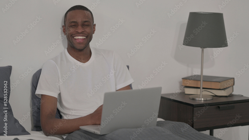 African Man Smiling at Camera while using Laptop in Bed African Man Smiling at Camera while using Laptop in Bed