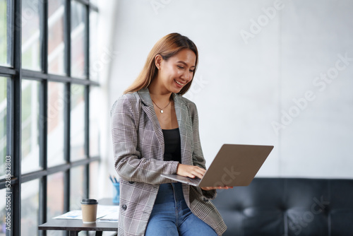 Beautiful Asian businesswoman standing and working on laptop with smiling face while working in office.