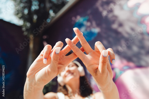 the girl makes a hashtag with her hands. a young woman wearing headphones shows a hashtag against the background of the street and graffiti