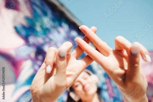 the girl makes a hashtag with her hands. a young woman wearing headphones shows a hashtag against the background of the street and graffiti