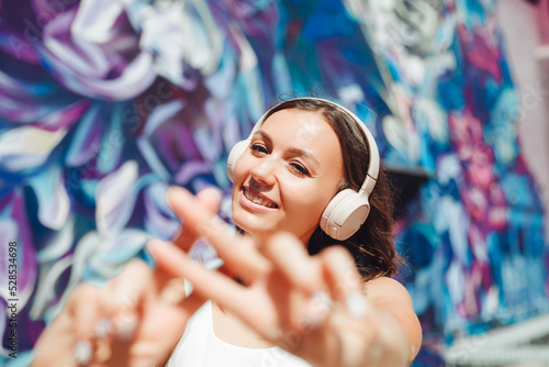 the girl makes a hashtag with her hands. a young woman wearing headphones shows a hashtag against the background of the street and graffiti
