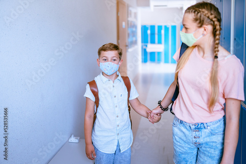 Back to school. Little brother and teenager sister, girl and boy in protective masks with school backpacks go to study after a pandemic, quarantine or coronavirus. First school day.