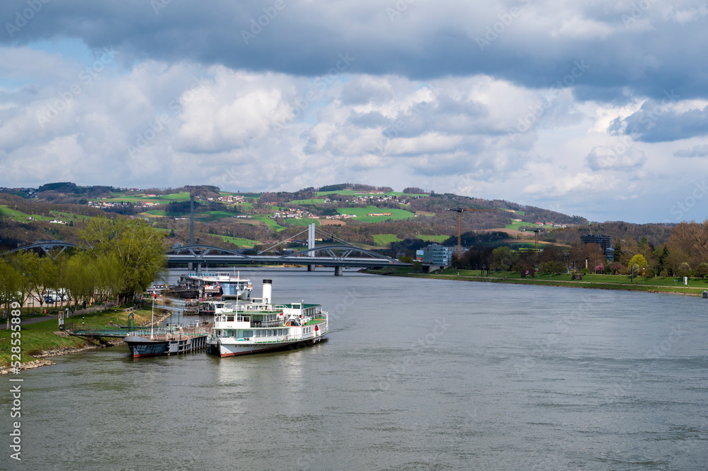 River Danube, boats and bridges between green meadows and forests near the city of Linz.