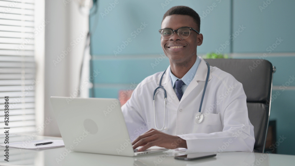Young African Doctor Smiling at Camera while using Laptop in Office Young African Doctor Smiling at Camera while using Laptop in Office
