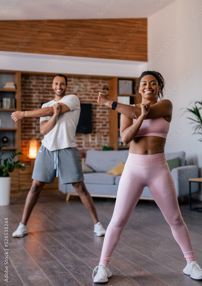 Obraz premium Smiling young african american male and female in sportswear doing stretching or warm up exercises for hands