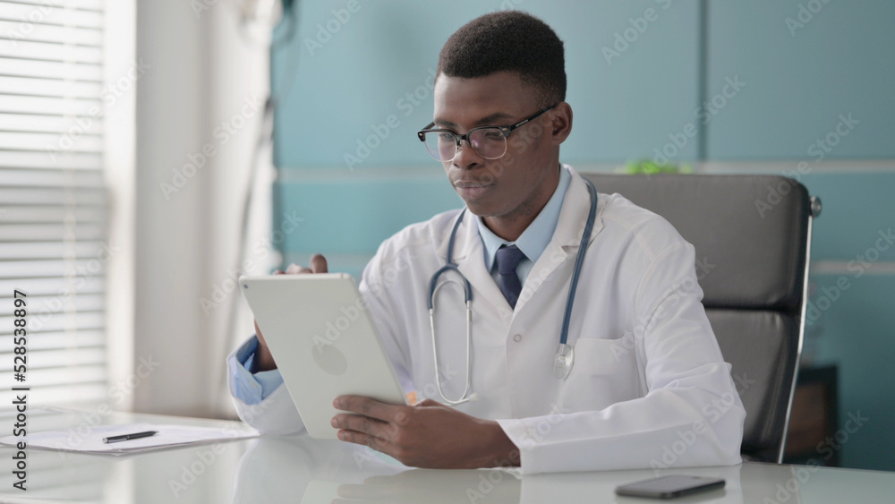 Young African Doctor using Tablet while Sitting in Office Young African Doctor using Tablet while Sitting in Office