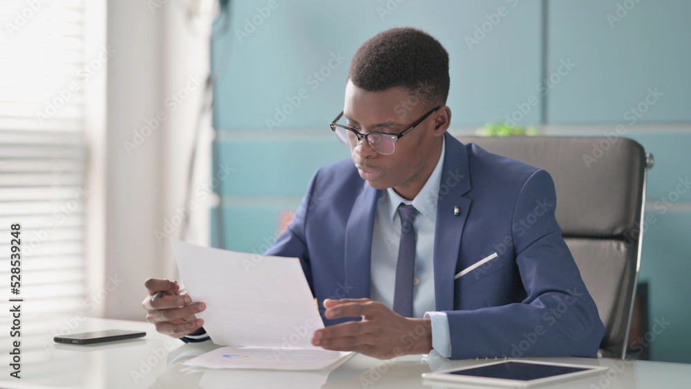 Young African Businessman Reading Reports while Sitting in Office