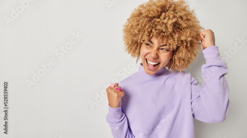 Fotografia Excited happy woman with curly bushy hair makes fist pump exclaims yes celebrate