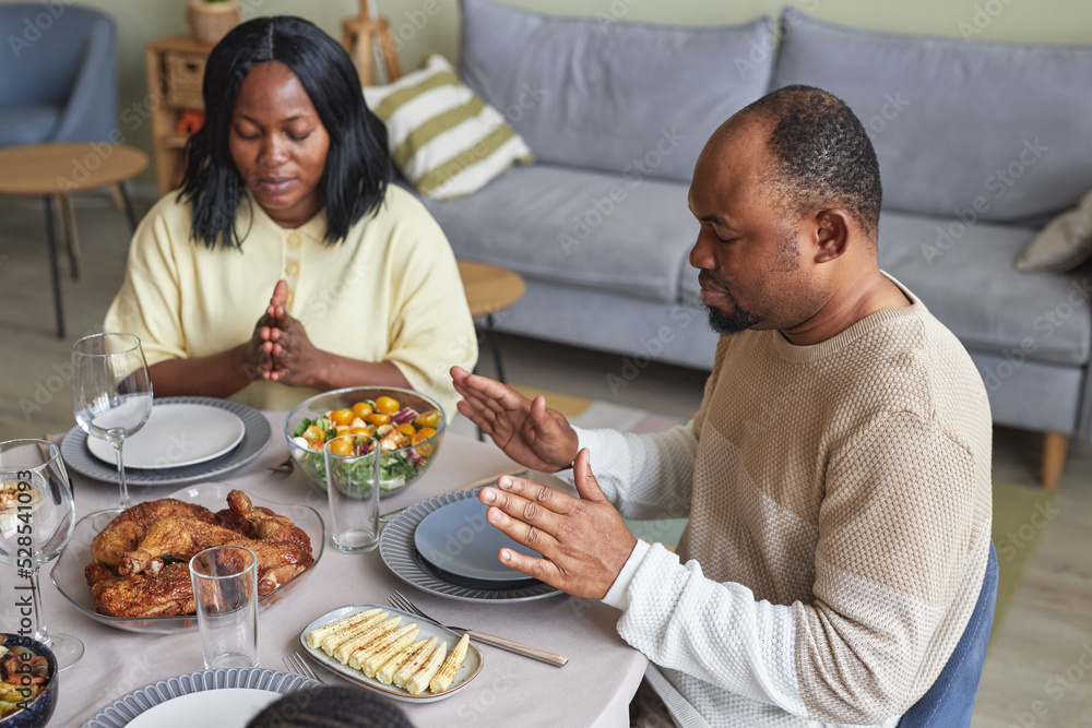 African young couple praying at dining table before dinner in living room African young couple praying at dining table before dinner in living room