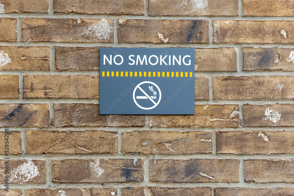 No smoking sign on the building, warning sign on the brick wall background, information about ban of smoking. No smoking sign on the building, warning sign on the brick wall background, information about ban of smoking.