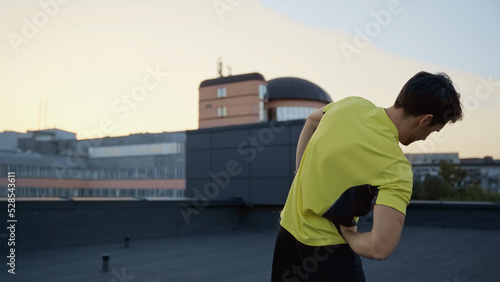 Young brunette sportsman working out on roof in evening.