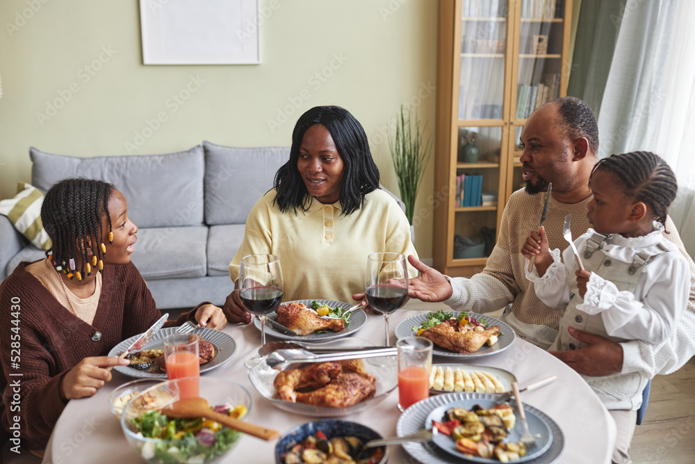 African family of four talking to each other while having dinner at table in living room African family of four talking to each other while having dinner at table in living room