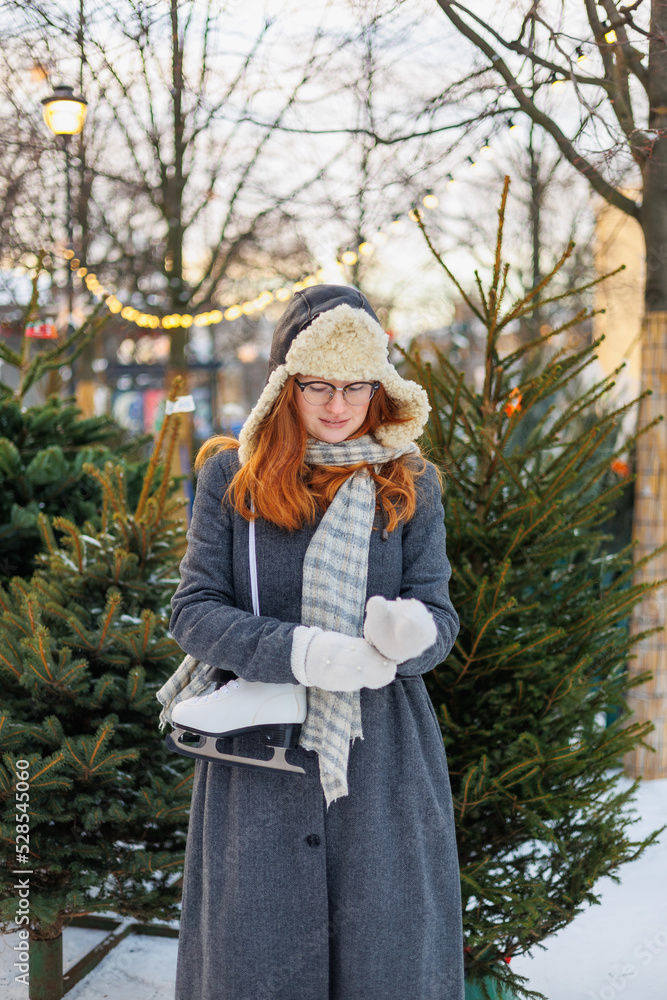 woman is resting and walking in the park in winter, a happy European woman with red hair is skating. a young and beautiful woman in a gray vintage coat is enjoying the Christmas holidays