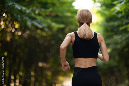 Back view of woman in sportswear jogging in park © Prostock-studio