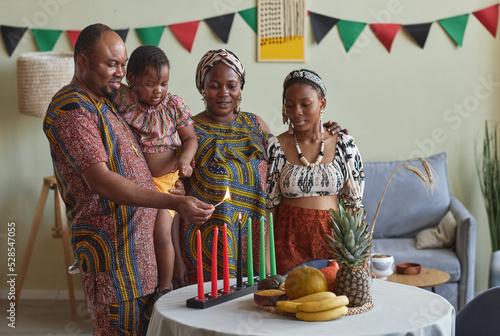 African family of four burning candles together to celebrate Kwanzaa holiday together at home photo