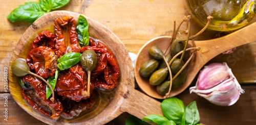 Capers and Dried tomatoes with herbs in olive oil.Large capers. Traditional appetizers in Italy with garlic, Provence herbs and basil. Ingredients for bruschetta and aperitif. top view