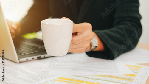Businessman holding a cup of coffee and drinking before work in the morning in front of a laptop.