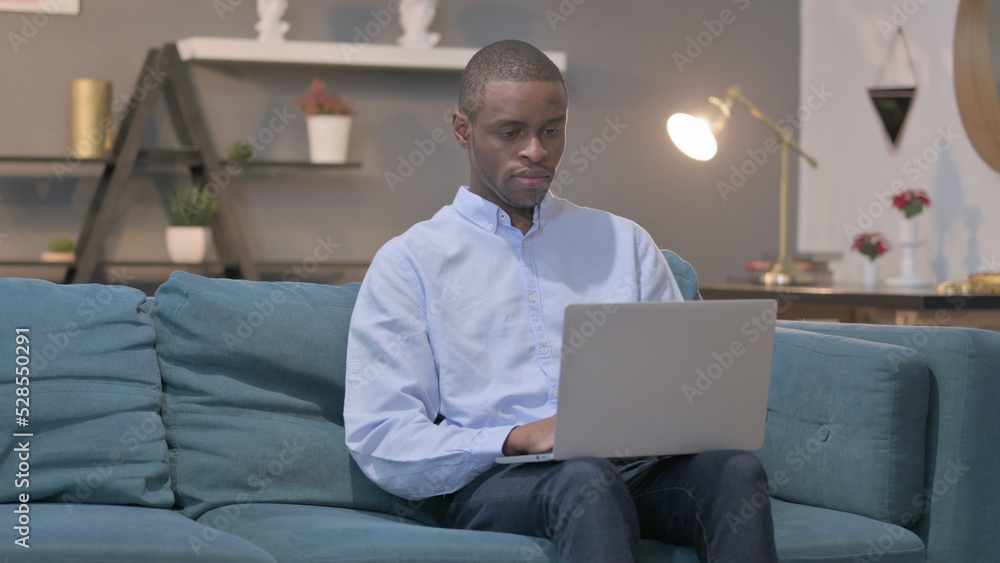 African Man Working on Laptop on Sofa African Man Working on Laptop on Sofa