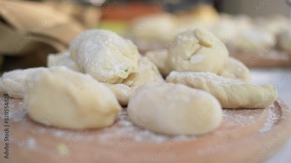 Selective focus. Close-up of homemade dumplings, Ukrainian varenyky on a wooden board, with changing focus to a saucepan with boiling water on an electric stove in the rustic summer country kitchen Selective focus. Close-up of homemade dumplings, Ukrainian varenyky on a wooden board, with changing focus to a saucepan with boiling water on an electric stove in the rustic summer country kitchen