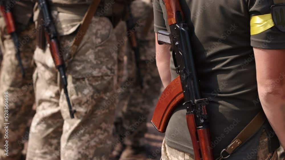 A row of Ukrainian soldiers line up at the checkpoint, wearing military uniforms and holding Kalashnikov assault rifles behind their backs. A row of Ukrainian soldiers line up at the checkpoint, wearing military uniforms and holding Kalashnikov assault rifles behind their backs.
