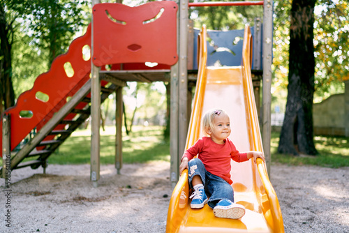 Tableau sur toile Little girl sits on the bottom of the slide on the playground