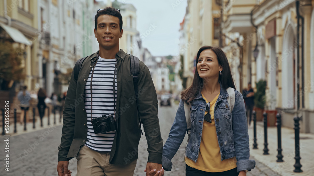 Smiling multiethnic tourists holding hands on urban street.