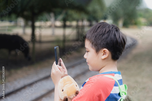 Photography School kid using mobile phone taking photo of animal in the cage in the farm, Ch