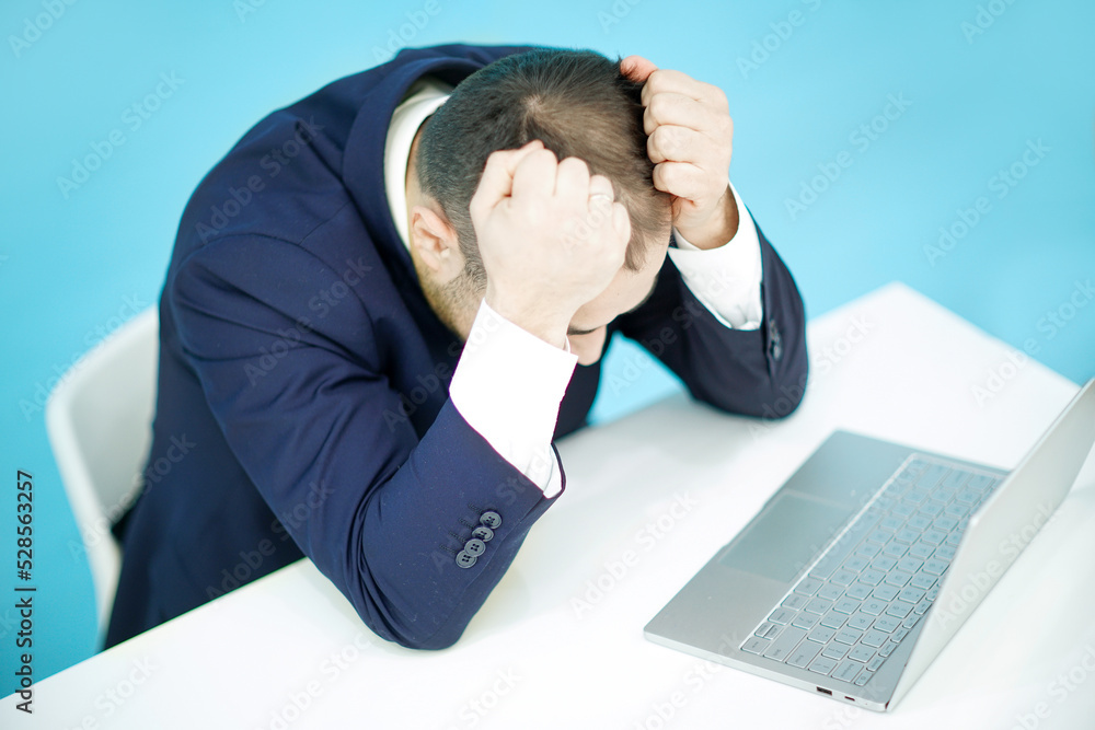A businessman holding his head looking at laptop. A businessman holding his head looking at laptop.