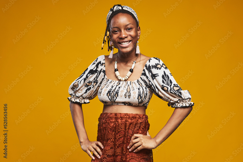 Portrait of African girl in national clothes smiling at camera standing against yellow background Portrait of African girl in national clothes smiling at camera standing against yellow background