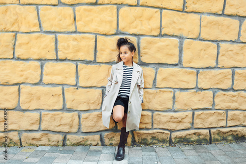 a little girl in a striped sweatshirt poses against a brick wall. children's autumn fashion. generation z