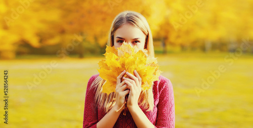 Portrait of beautiful happy smiling blonde woman with yellow maple leaves in autumn park