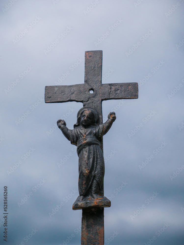 Iron cross in cemetery with small jesus with blue sky background
