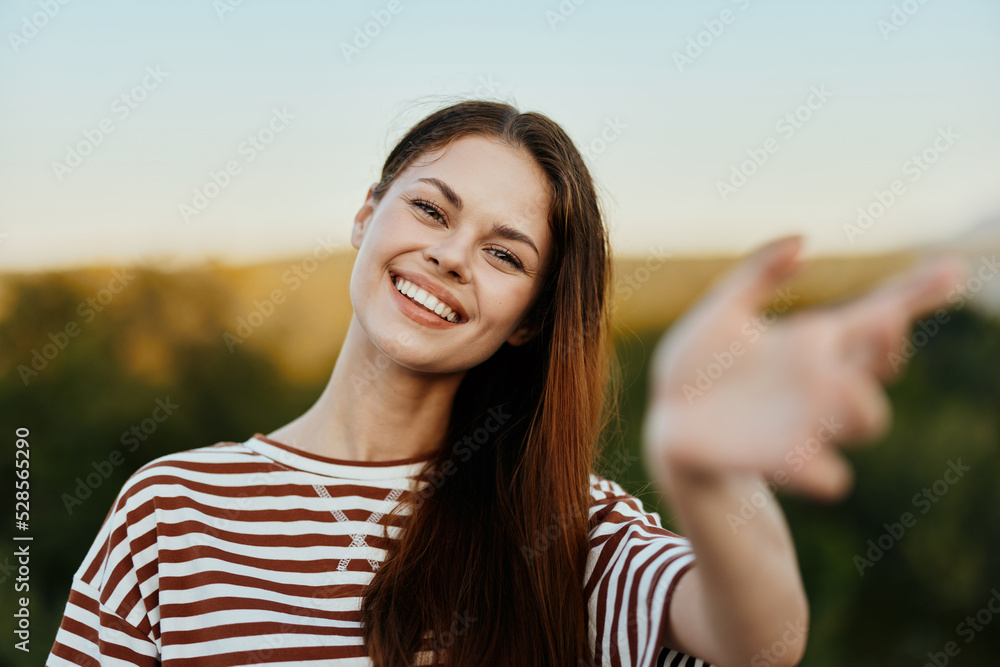 Woman smiling while looking at the camera and pulling her hands to the camera close-up in nature with a view of the mountains. Happy travel lifestyle follow me