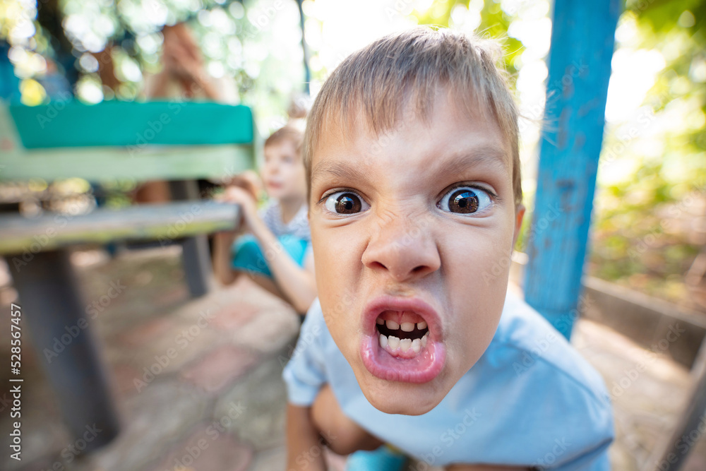 Angry young boy making grimace and expressing aggression - obrazy, fototapety, plakaty 