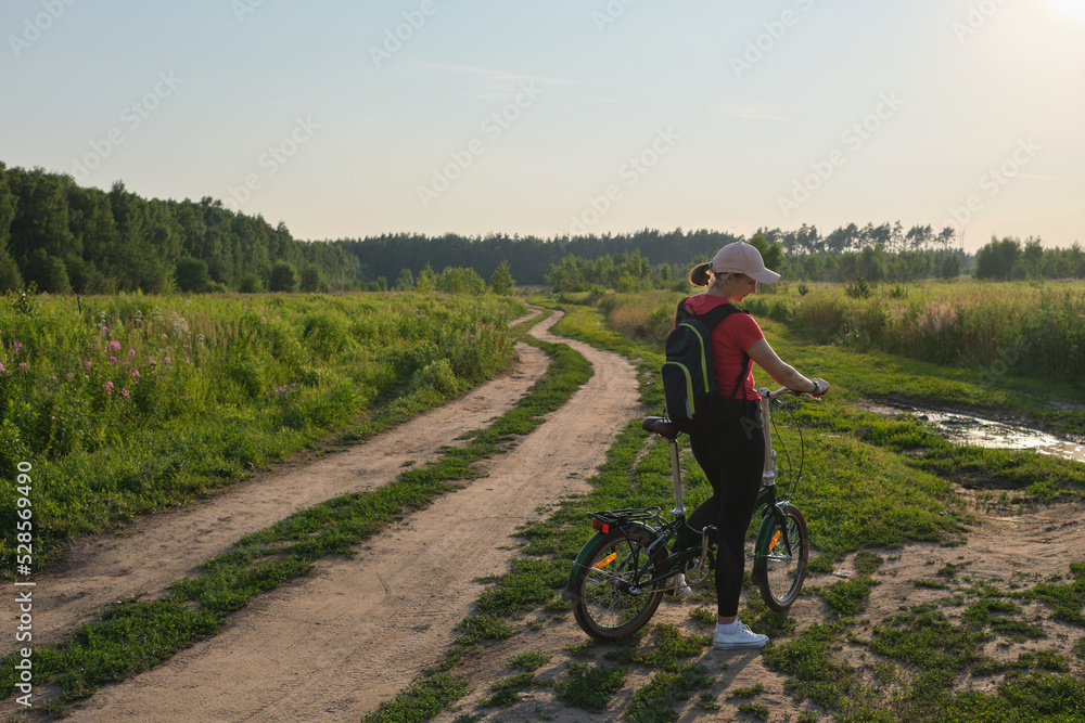 Young woman standing with bicycle and enjoying sunset in the countryside. Healthy lifestyle concept.